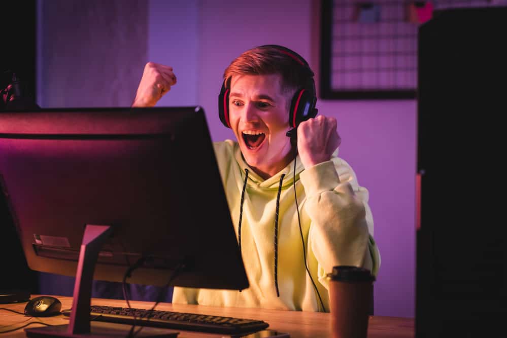Excited gamer in headset showing yeah gesture near computer